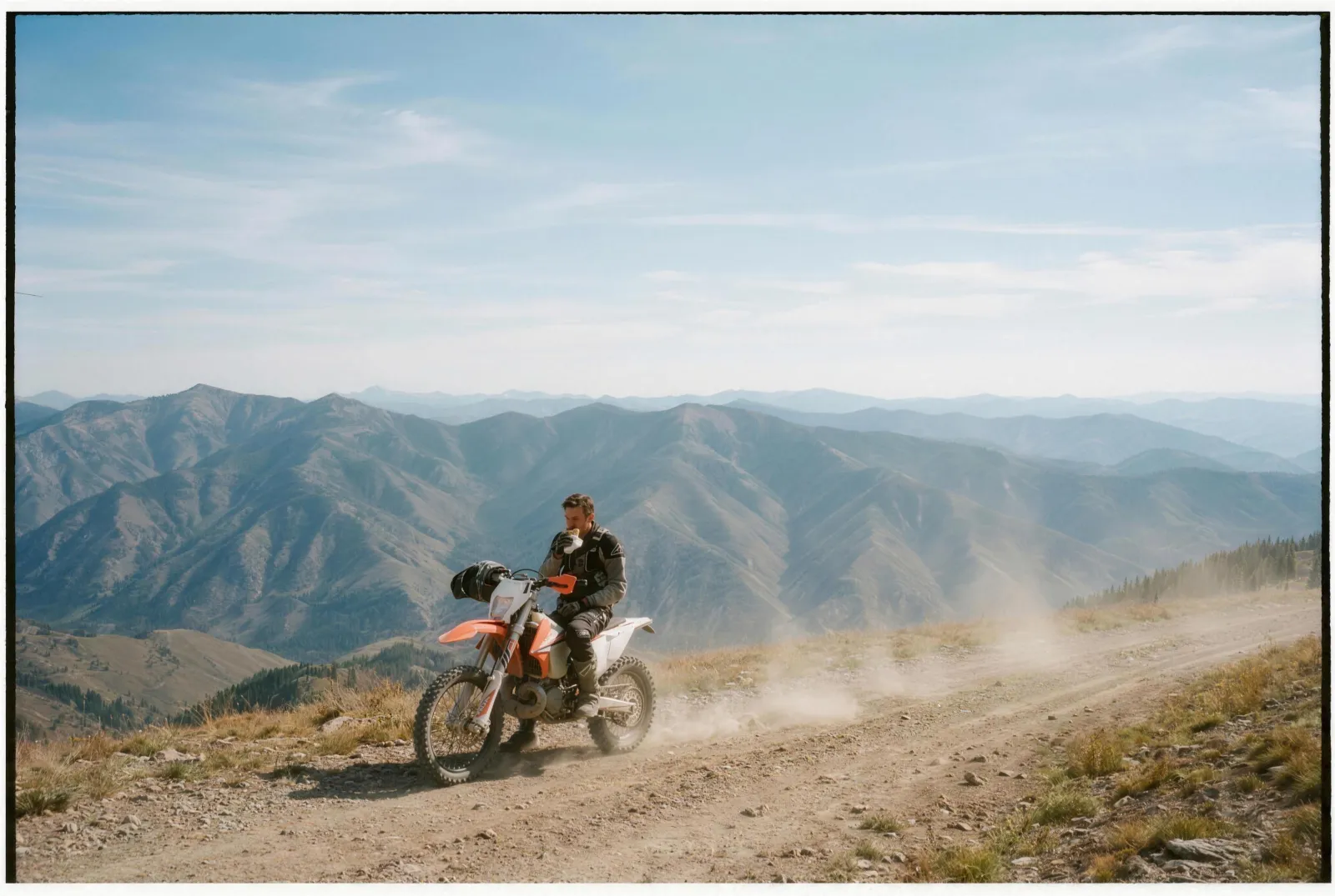 A dirt-bike rider eating a Rut'n Buck breakfast burrito on a Montana mountain ridge