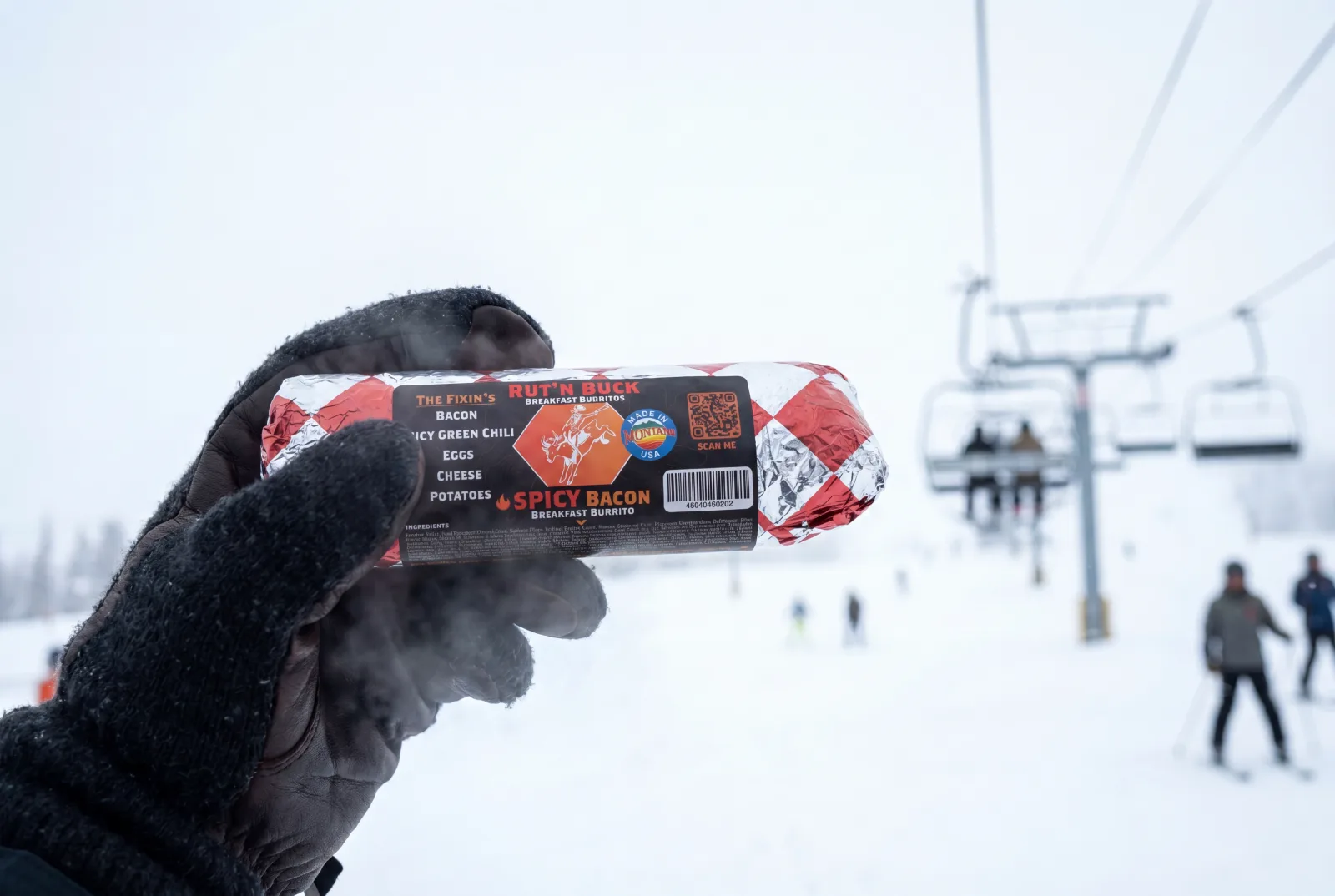 A gloved hand holding a Rut'n Buck burrito on a ski day