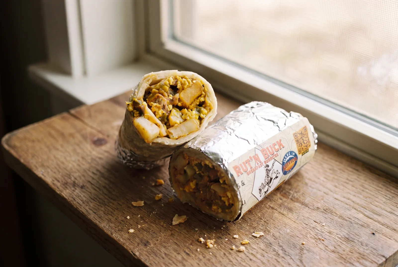 A Southwest vegetarian breakfast burrito cut open, showing sweet corn, black beans, potatoes, cheese, and green chili