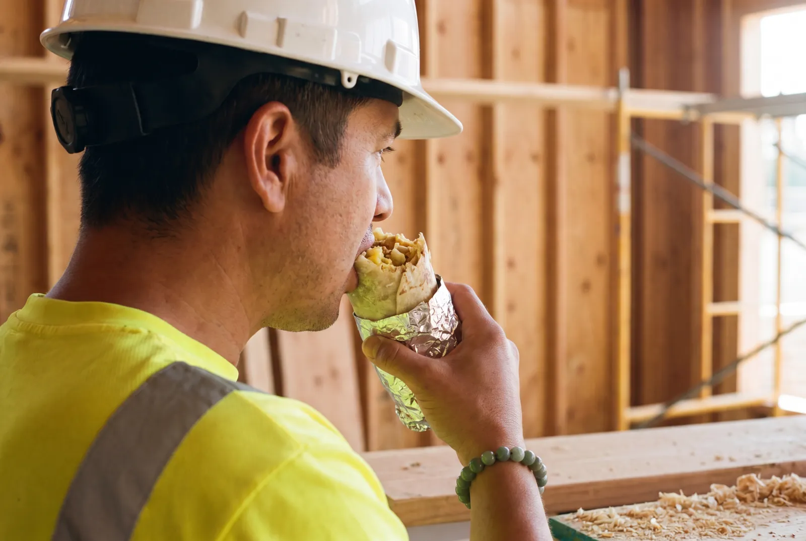 A hard-hat worker mid-bite of a Rut'n Buck breakfast burrito on a jobsite