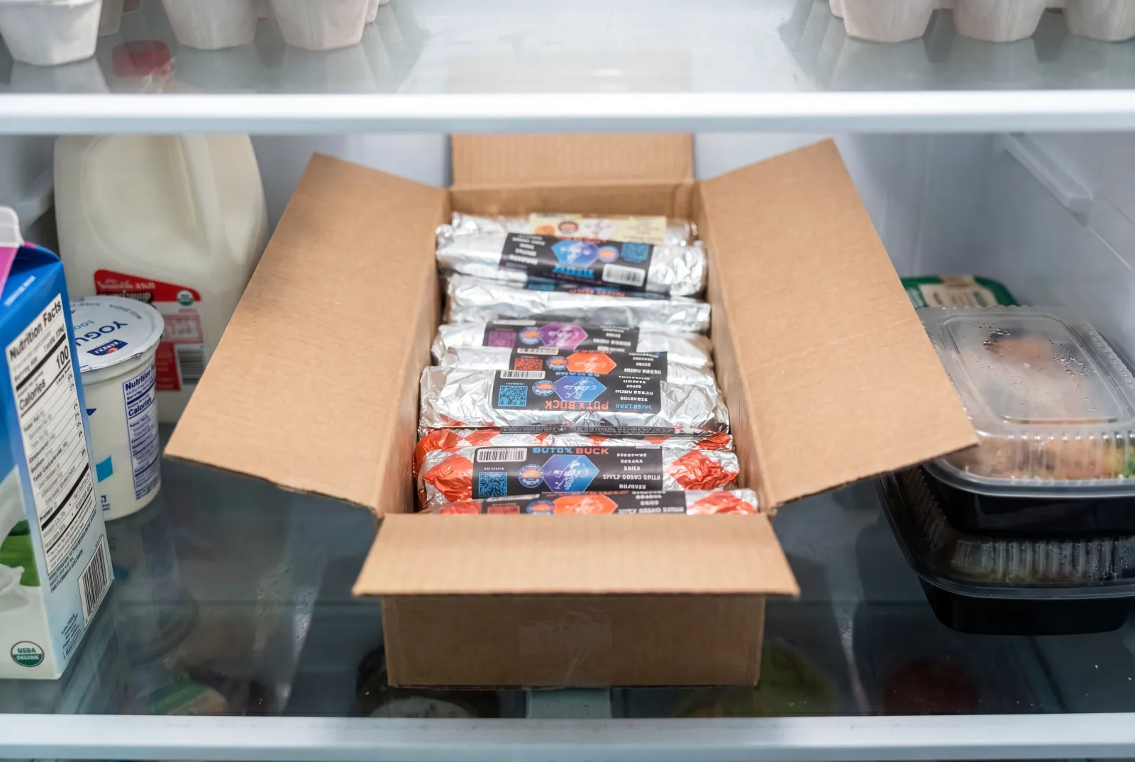 An open box packed with rows of foil-wrapped Rut'n Buck breakfast burritos, dropped on a standing program order