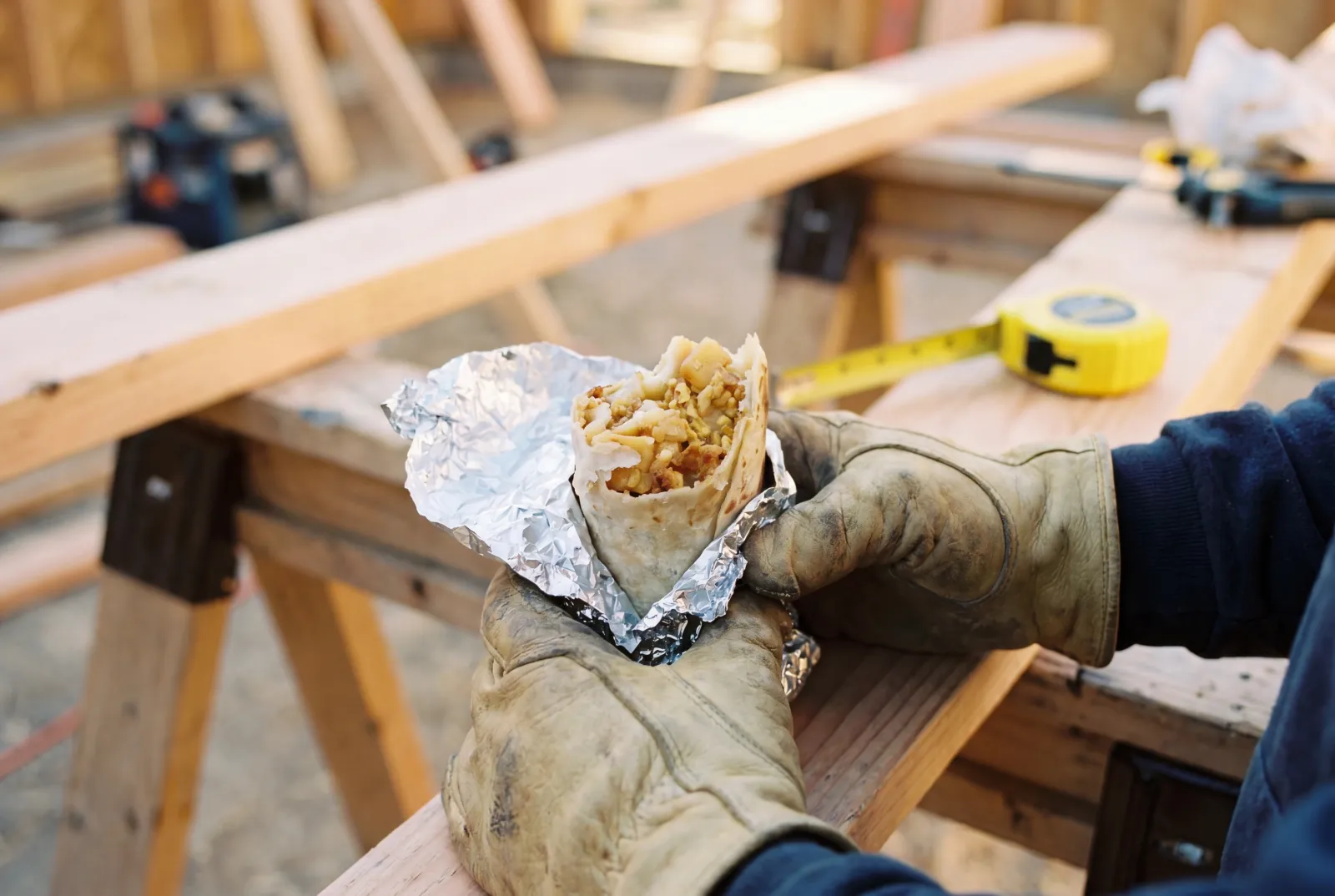 Gloved hands holding a foil-peeled Rut'n Buck breakfast burrito on a sawhorse